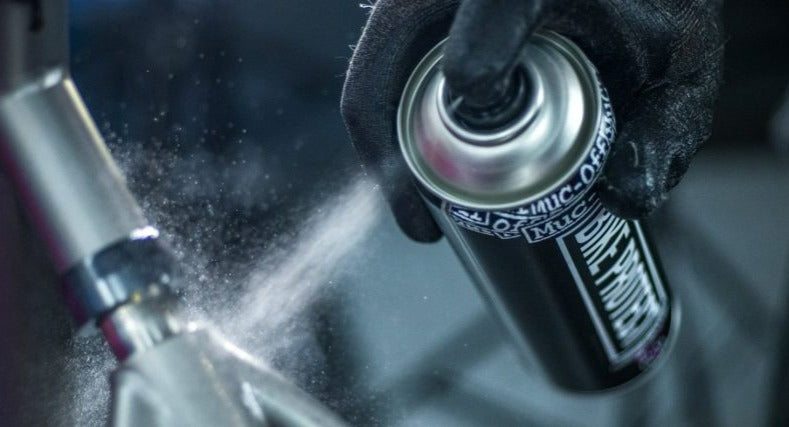 Gloved hand spraying bike cleaner onto a frame