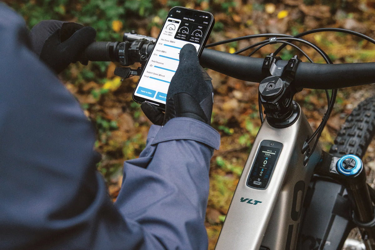 Limited time: Norco fluid vlt clear-out! A close-up outdoor shot of a person holding a smartphone mounted on a Norco VLT bike handlebar.